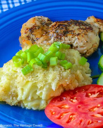 Bright blue plate filled with a piece of chicken, sliced zucchini, an heirloom tomato, large scoop of Cheesy Chile Rice Casserole topped with sliced green onions, with a blue checked cloth in the back and a fork in front © 2026 Jane Bonacci, The Heritage Cook.