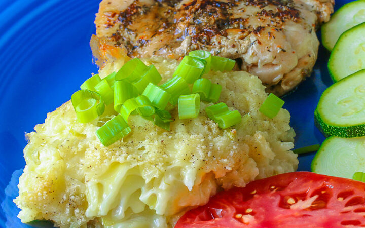 Bright blue plate filled with a piece of chicken, sliced zucchini, an heirloom tomato, large scoop of Cheesy Chile Rice Casserole topped with sliced green onions, with a blue checked cloth in the back and a fork in front © 2026 Jane Bonacci, The Heritage Cook.