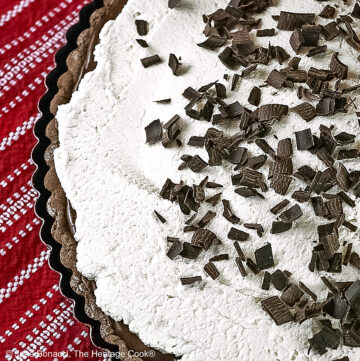 Chocolate Mocha Tart the whole tart, with the chocolate filling covered with a whipped topping and sprinkled with shaved chocolate pieces, some with a slice on a plate in front of the rest of the tart on red and white cloths © 2025 Jane Bonacci, The Heritage Cook.