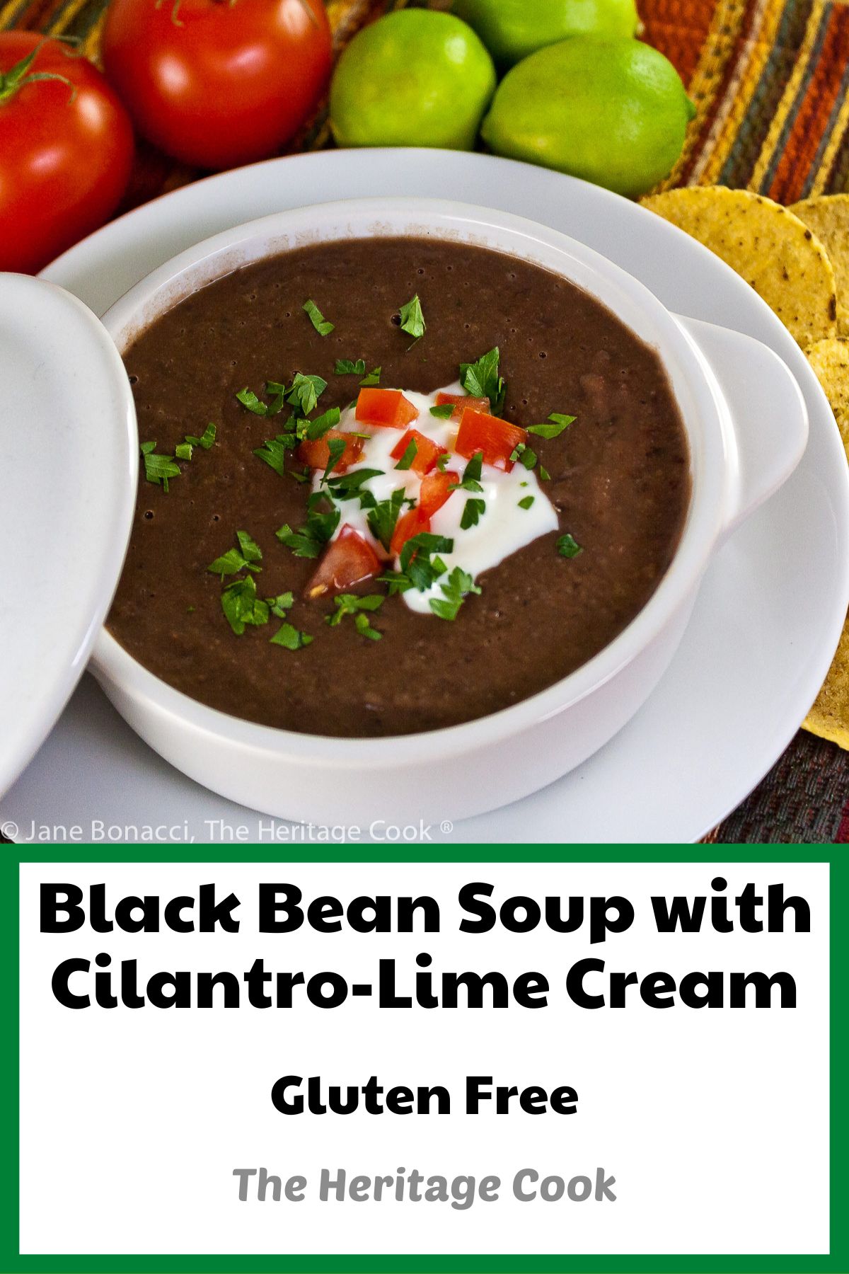 Dark black bean soup in white bowls garnished with cream, tomatoes, and chopped cilantro and lime slices, with tortilla chips alongside; Chipotle Black Bean Soup with Cilantro Lime Cream (GF) © 2023 Jane Bonacci, The Heritage Cook. 