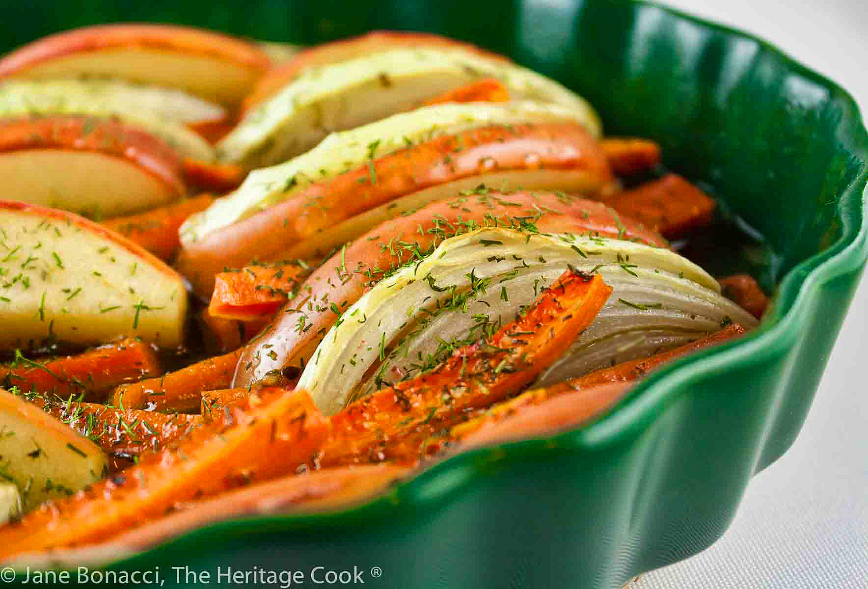 Carrots, apples, and onions sliced and tucked into layers in a green au gratin dish roasted with a maple glaze © 2023 Jane Bonacci, The Heritage Cook. 