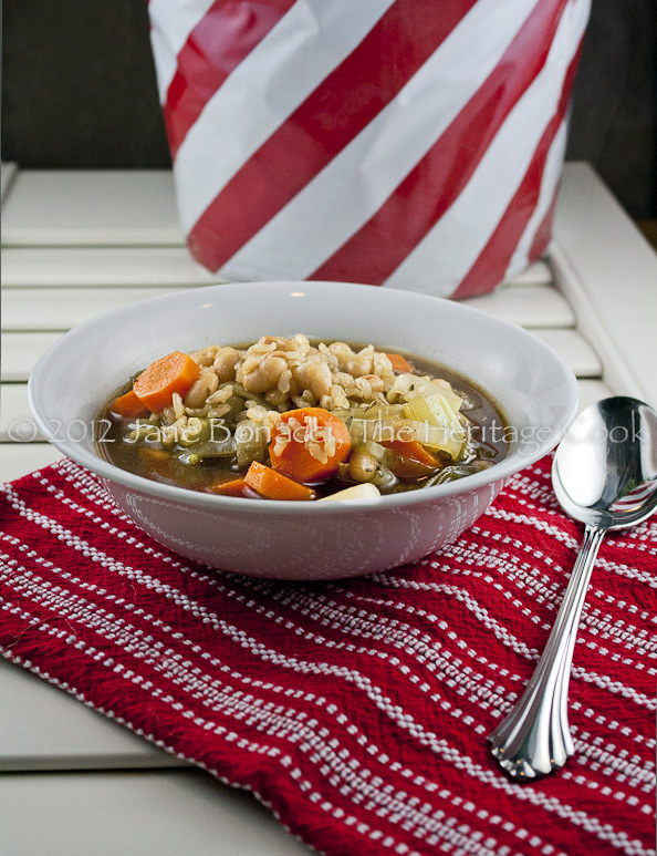 Bowl of soup on deep red towel with candy-stripe pot of rosemary in background