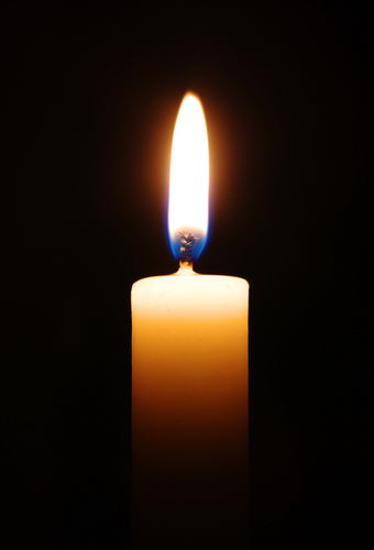 Single burning candle surrounded by blackness