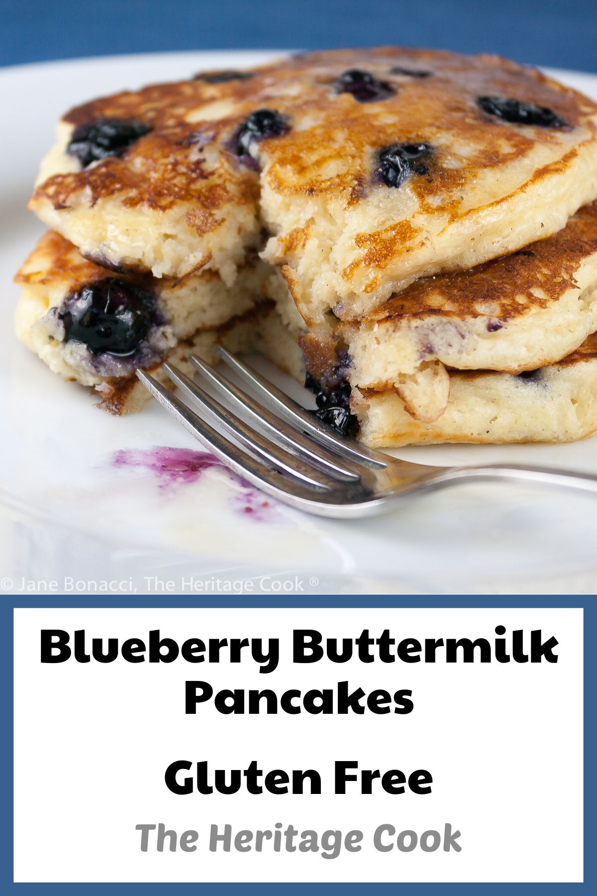 Stack of three blueberry pancakes on white plate with blue background; Blueberry Buttermilk Pancakes © 2023 Jane Bonacci, The Heritage Cook. 