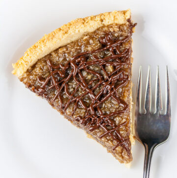 Coconut Caramel Cookie Tart that tastes like a Samoa Girl Scout Cookie; beautiful wedge of the tart drizzled with chocolate and ready to dive into © 2023 Jane Bonacci, The Heritage Cook.