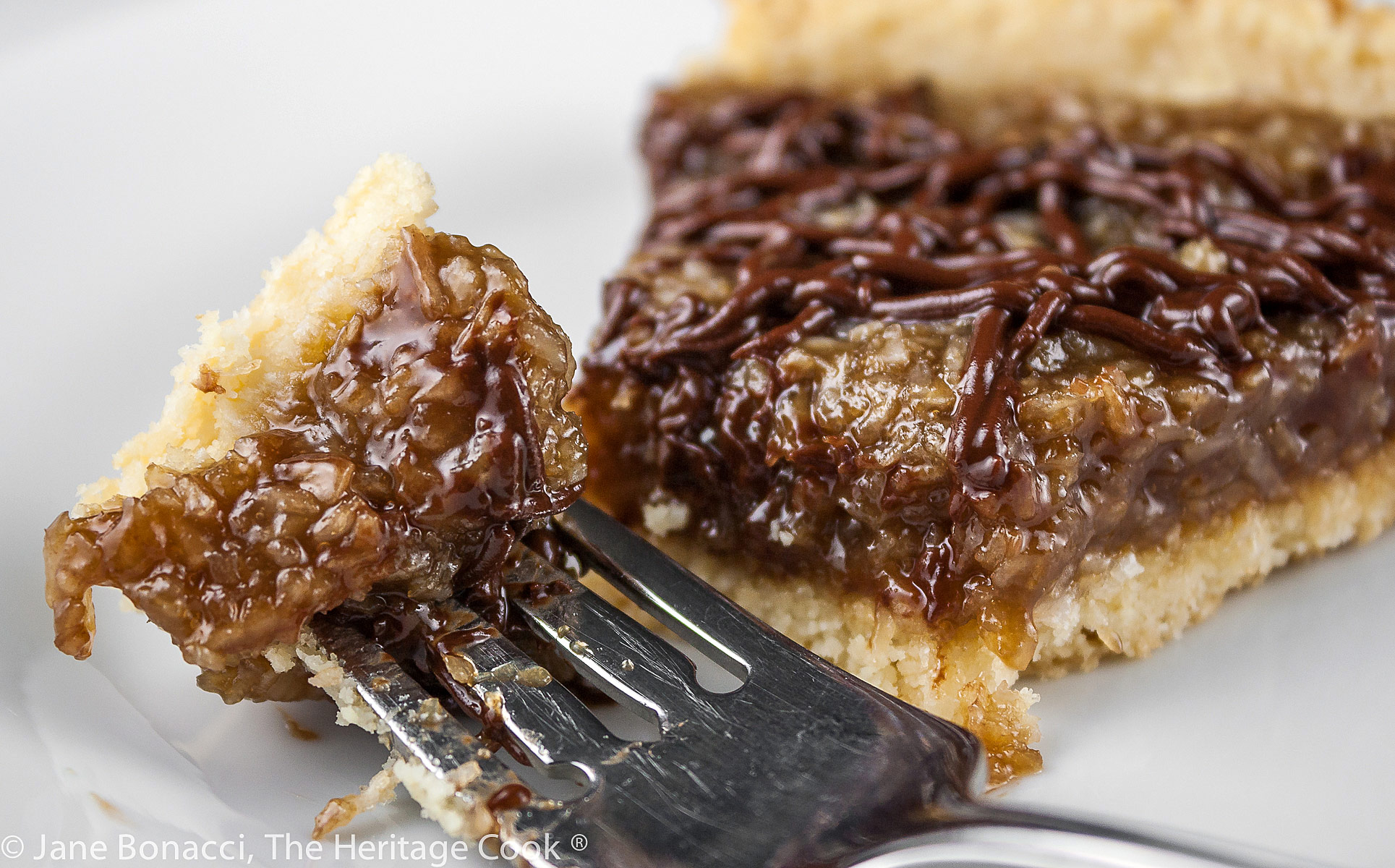 Coconut Caramel Cookie Tart that tastes like a Samoa Girl Scout Cookie; beautiful wedge of the tart drizzled with chocolate and ready to dive into © 2023 Jane Bonacci, The Heritage Cook.