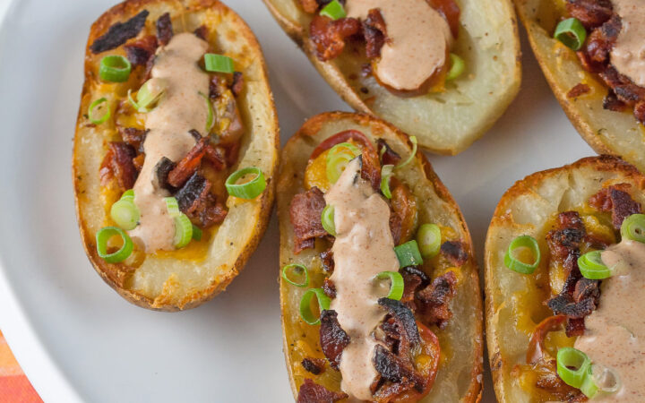 Baked potatoes are split lengthwise with the centers hollowed out and filled with crumbled bacon, green chiles, tomatoes, and melted cheese. Topped with green onions and a drizzle of taco cream. Served with lime wedges. © 2023 Jane Bonacci, The Heritage Cook.