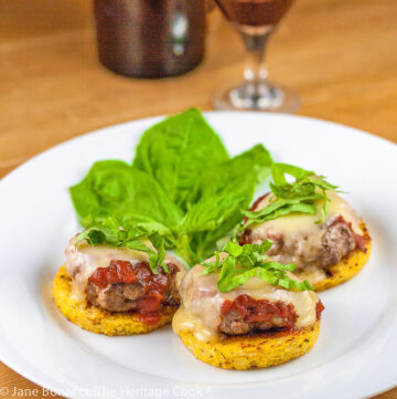 Mini burger patties on firm polenta circles, topped with fresh marinara sauce and melted cheese, then sprinkled with basil. Italian Sliders with Polenta and Marinara (Gluten Free); © 2023 Jane Bonacci, The Heritage Cook.