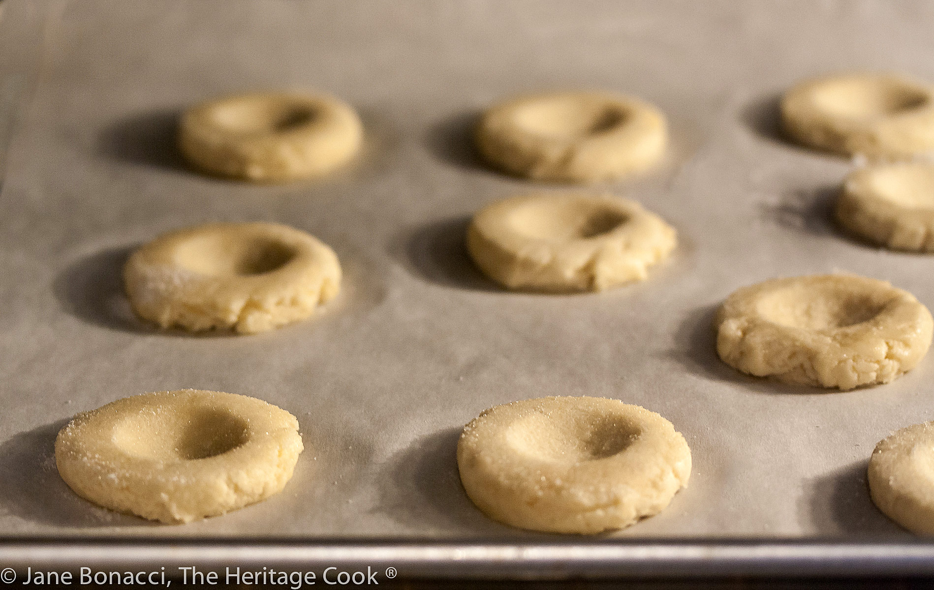 Cookie dough on parchment paper lined baking sheet, each one with a divot pressed in the center of each one. 