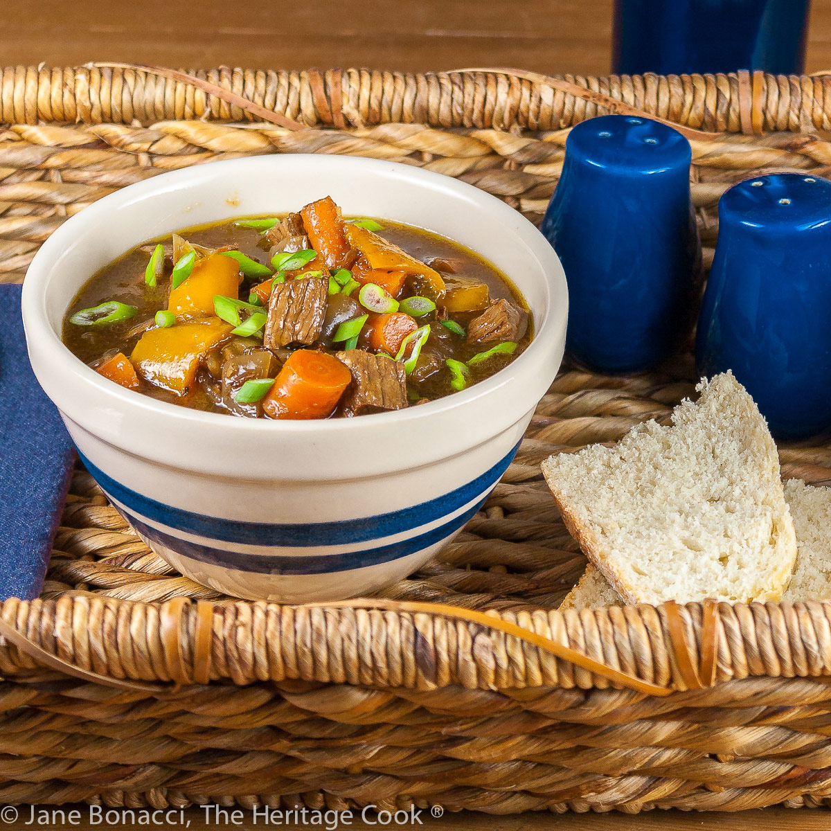 Blue and white striped bowl with blue napkin in a woven basket; Old-Fashioned Beef Stew and Valentine's Day Love Story © 2023 Jane Bonacci, The Heritage Cook.