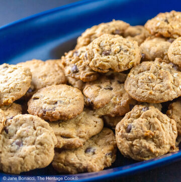 Long oval dark blue platter piled high with perfectly baked peanut butter, chocolate chip, and oatmeal cookies on a black background © 2025 Jane Bonacci, The Heritage Cook.