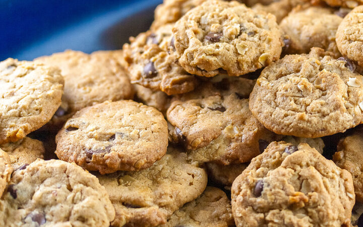 Long oval dark blue platter piled high with perfectly baked peanut butter, chocolate chip, and oatmeal cookies on a black background © 2025 Jane Bonacci, The Heritage Cook.