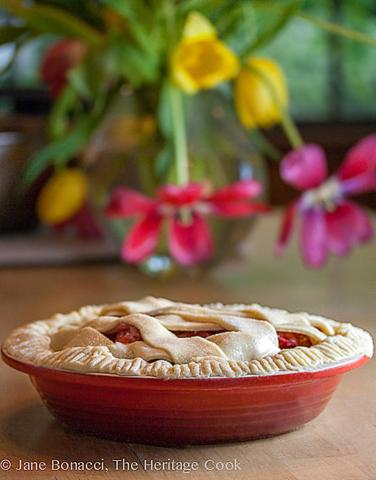 Strawberry-Rhubarb pie in red pie plate in front of bright tulips