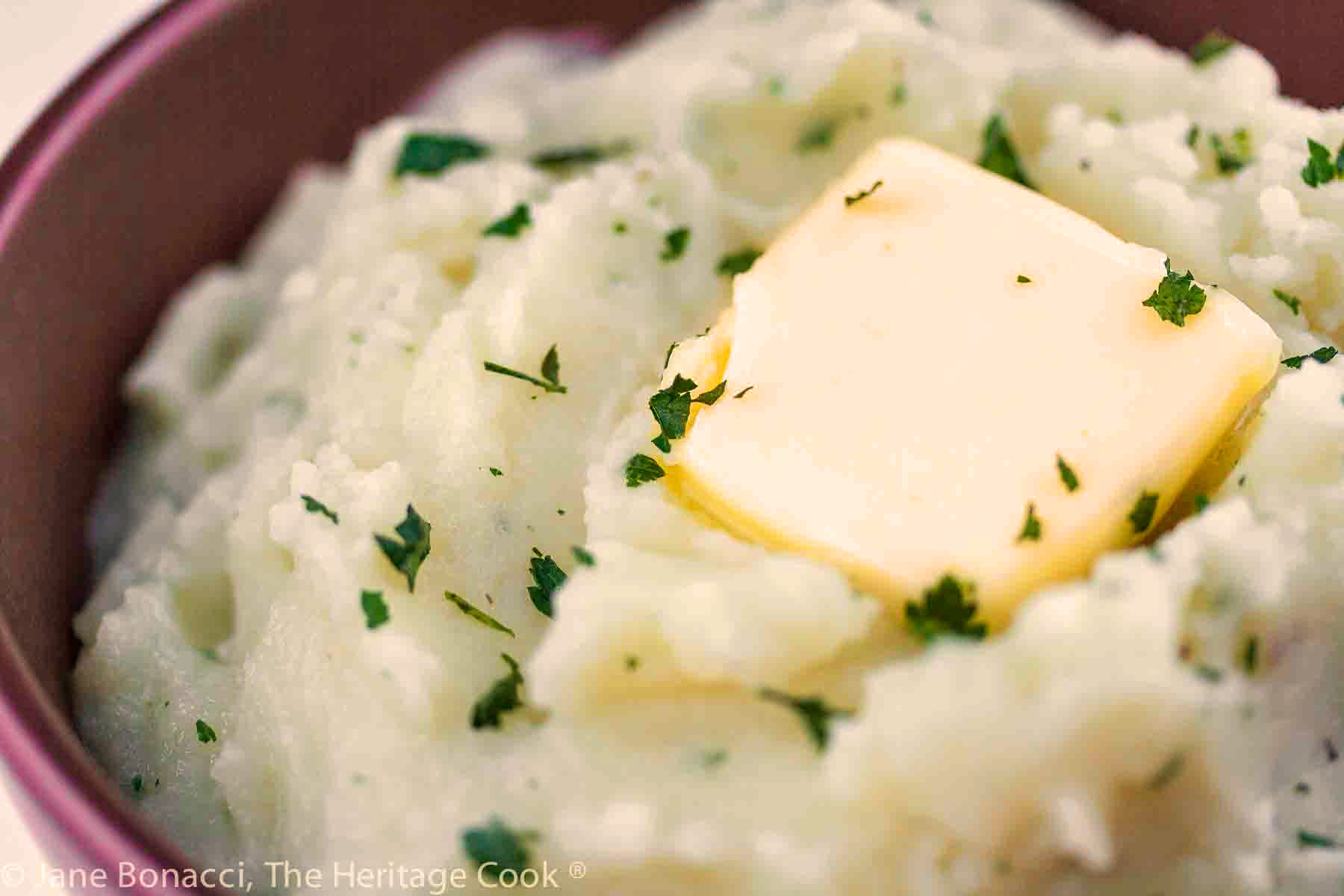 Bowl of piping hot mashed potatoes with a pat of butter on top and sprinkled with chopped parsley.