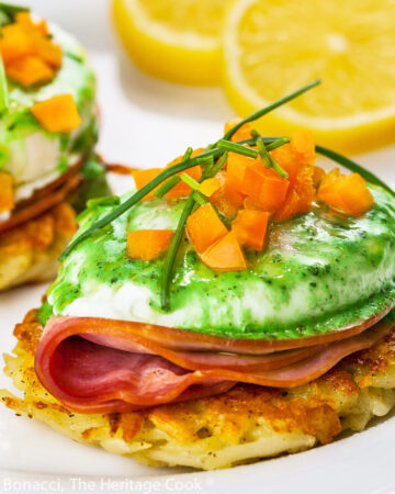 Potato pancakes topped with a slice of ham, a poached egg, basil hollandaise sauce, finely chopped orange bell peppers, and chives; Irish Hash Browns Benedict with Basil Hollandaise; © 2023 Jane Bonacci, The Heritage Cook.