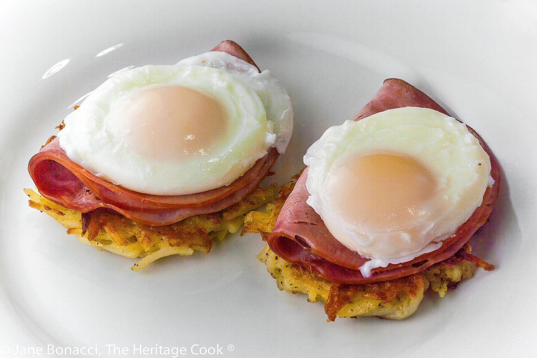 Two perfectly cooked eggs on ham slices and fried potato patties. 