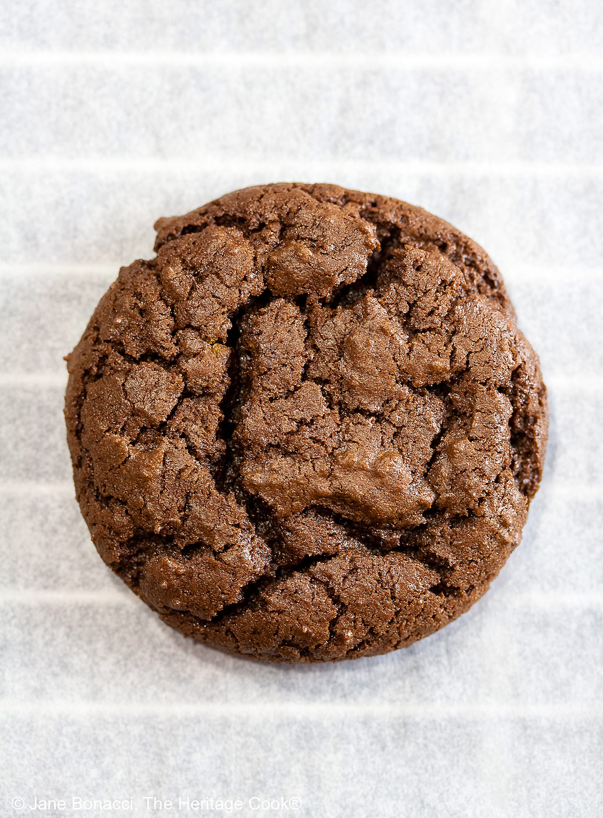 A single cookie, cooling on parchment paper over a wire rack.