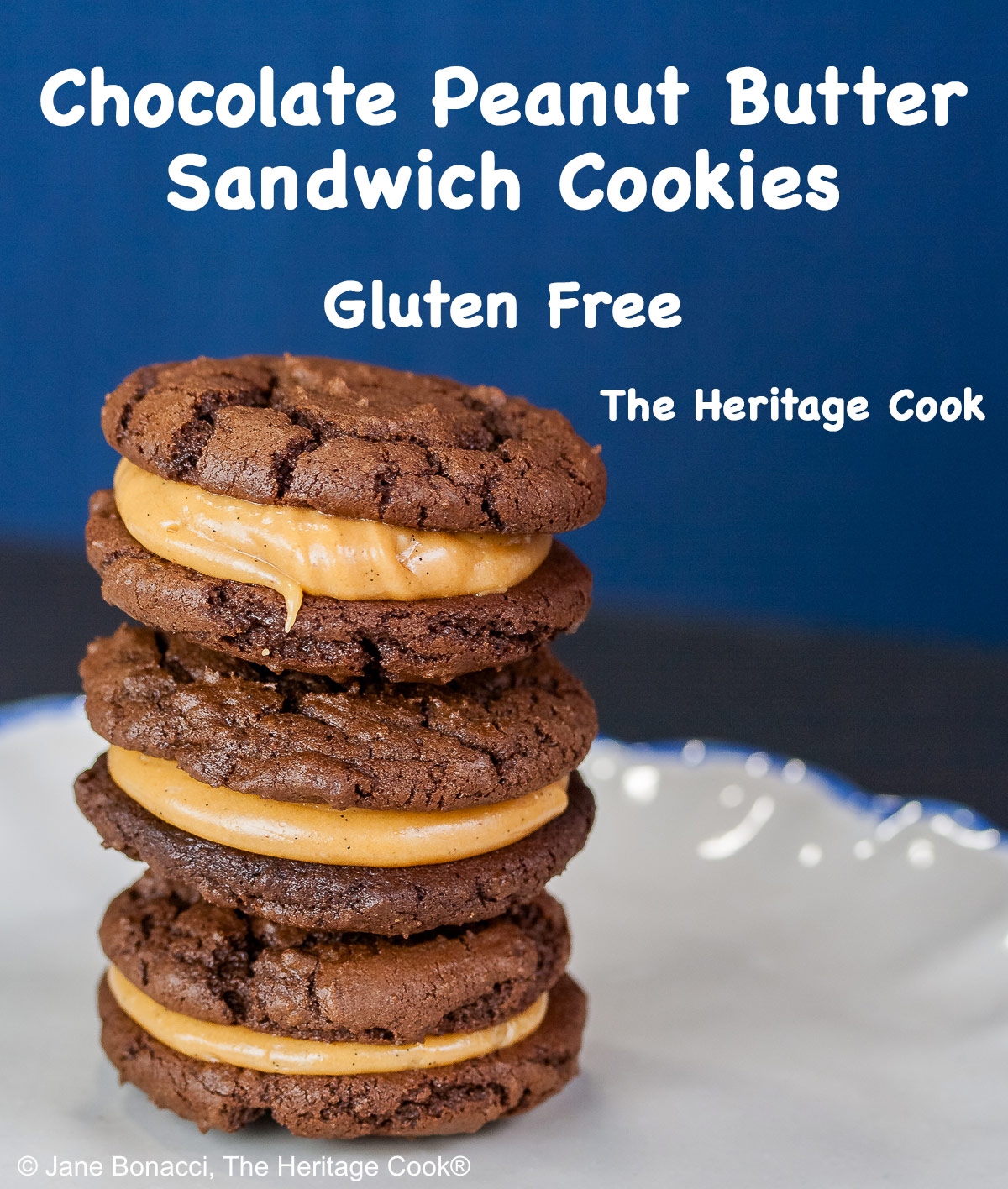 Stacks of Chocolate Peanut Butter Sandwich Cookies on a white plate with a scalloped blue edge, on a dark blue background some with a bowl of the filling to the side and a cloth with the Eiffel Tower on it behind © 2026 Jane Bonacci, The Heritage Cook.