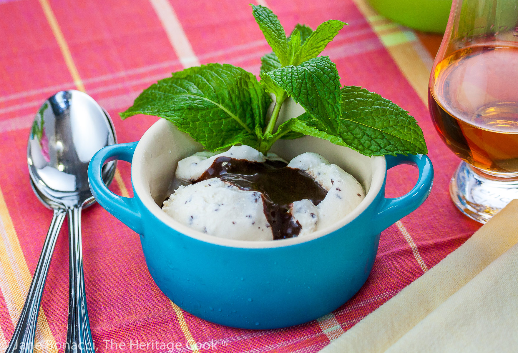 Ice cream in blue and green bowls topped with the chocolate sauce and a sprig of mint on a pink and orange cloth; Mint Julep Sundaes with Chocolate Bourbon Sauce (Gluten Free) © 2023 Jane Bonacci, The Heritage Cook. 