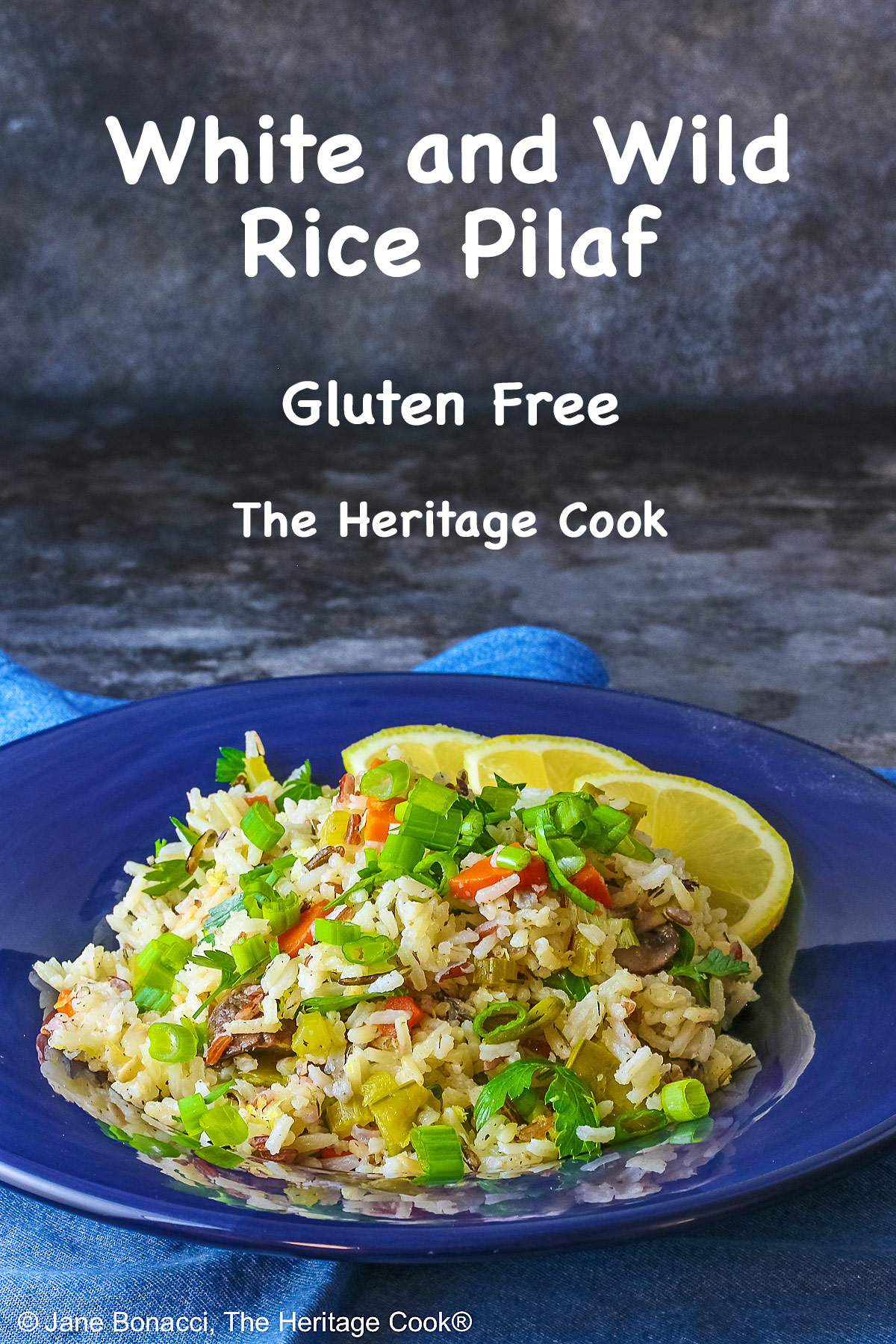 White and Wild Rice Pilaf with tons of vegetables is piled high in a deep blue bowl with a wide rim, topped with parsley and sliced green onions with three lemon slices along one edge © 2025 Jane Bonacci, The Heritage Cook.
