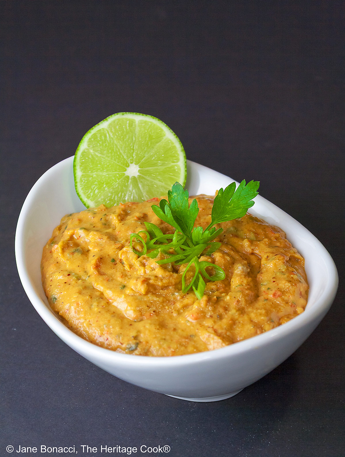 Bowl of Hummus Aioli with parsley sprig and lime slice. 