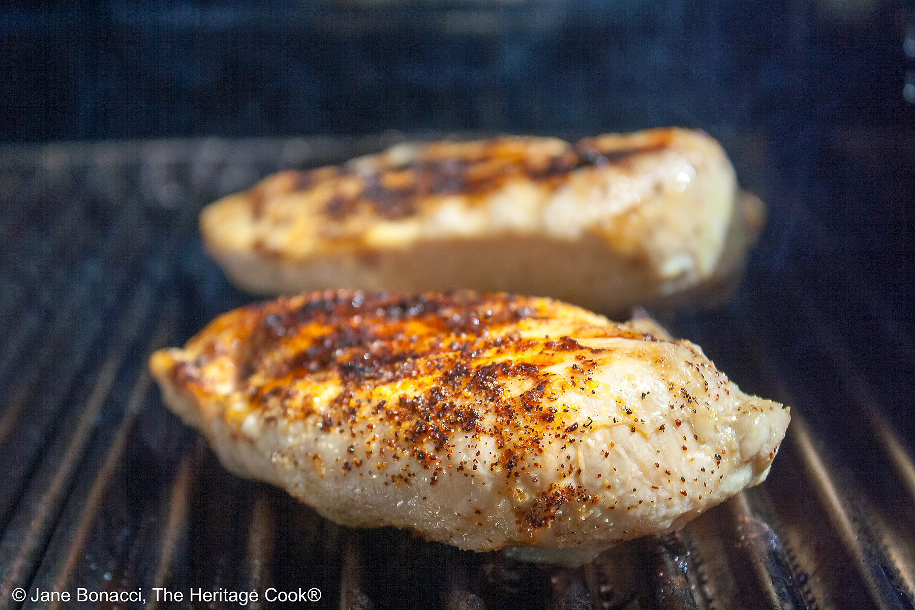 Two boneless chicken breasts on a BBQ grill with grill marks. 