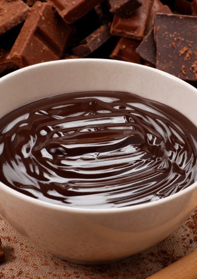 Bowl of melted chocolate with chopped chocolate and wooden spoon