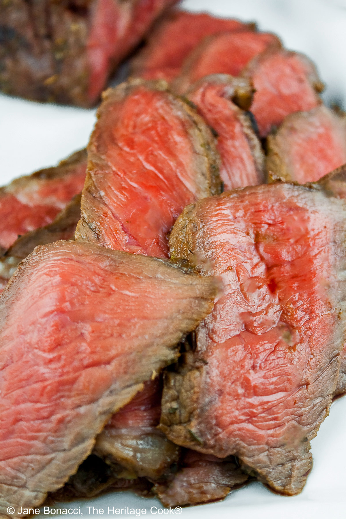 Pile of medium-rare sliced steak on a white plate. 