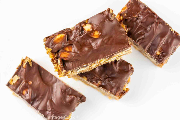 Layers of almond crust, caramel with nuts, topped with chocolate ganache cut into rectangles and stacked on a white oval plate © 2024 Jane Bonacci, The Heritage Cook.