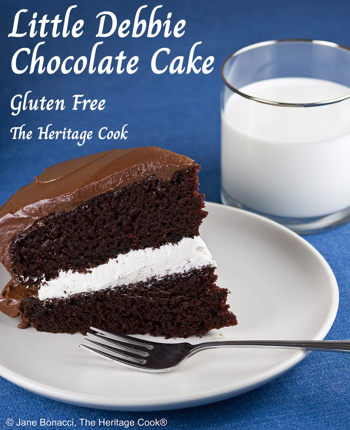 Slice of the Little Debbie Chocolate Layer Cake with vanilla filling on a white plate with a fork beside it, with a glass of milk behind and the whole cake with the slice cut out in the background © 2026 Jane Bonacci, The Heritage Cook.