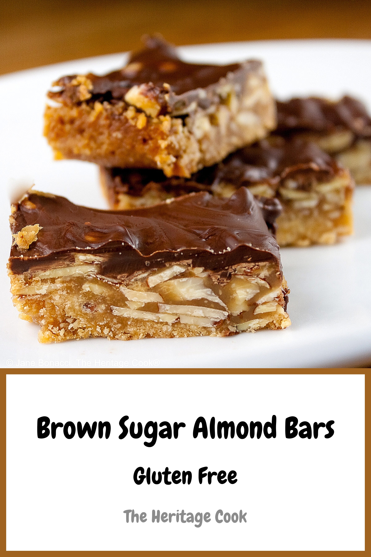 Luscious Brown Sugar Almond Bars, layered with a bottom crust, caramel filling, and topped with melted chocolate, stacked or scattered on a white plate, sitting on a golden wooden table © 2025 Jane Bonacci, The Heritage Cook.