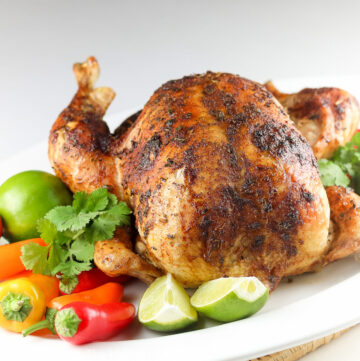 Golden brown roast chicken on white platter surrounded by brightly colored peppers, limes, and cilantro; Peruvian Roast Chicken, Gluten-Free © 2022 Jane Bonacci, The Heritage Cook.