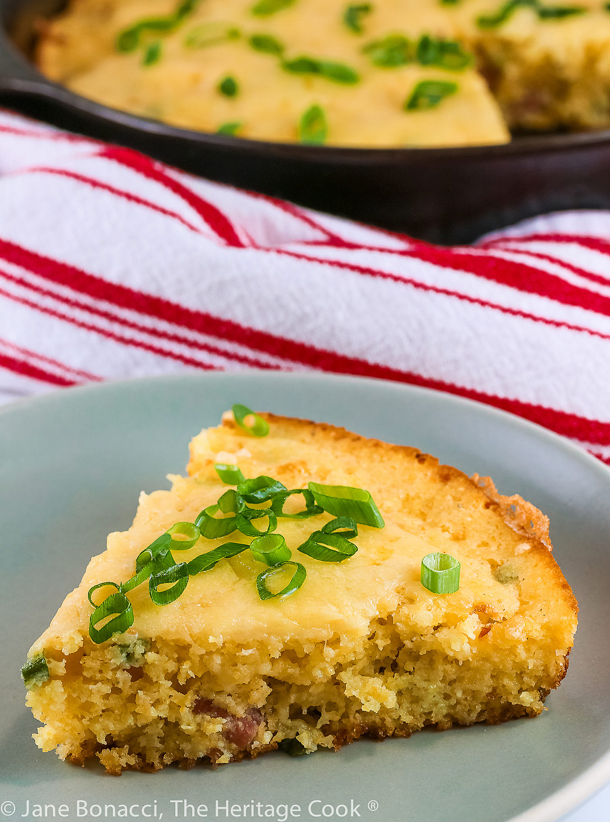 Ham and Cheese Cornbread baked in a cast iron skillet, slices on a small plate topped with sliced green onions © 2023 Jane Bonacci, The Heritage Cook.