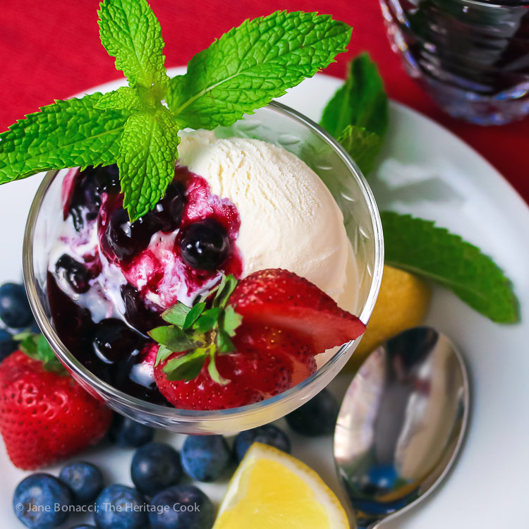 Top down on sundae with homemade fresh blueberry sauce, mint sprigs, sliced strawberry and lemon wedge; Ice Cream Sundae with Fresh Homemade Blueberry Syrup © 2017 Jane Bonacci, The Heritage Cook