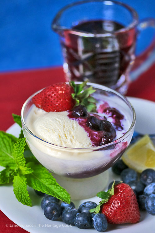 Blueberry and vanilla ice cream sundae in front with glass pitcher of the blueberry sauce behind it; Ice Cream Sundae with Fresh Homemade Blueberry Syrup © 2017 Jane Bonacci, The Heritage Cook