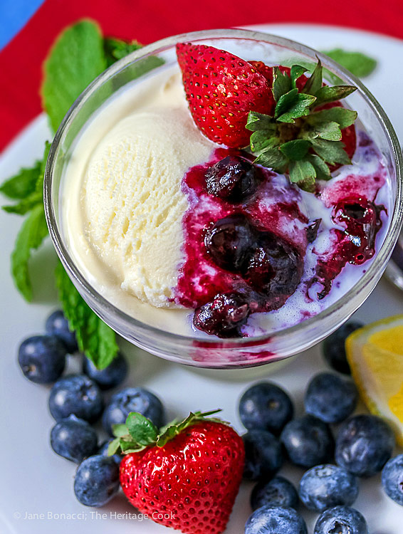 Bowl of vanilla ice cream topped with homemade fresh blueberry sauce surrounded with fresh blueberries, strawberries for 4th of July