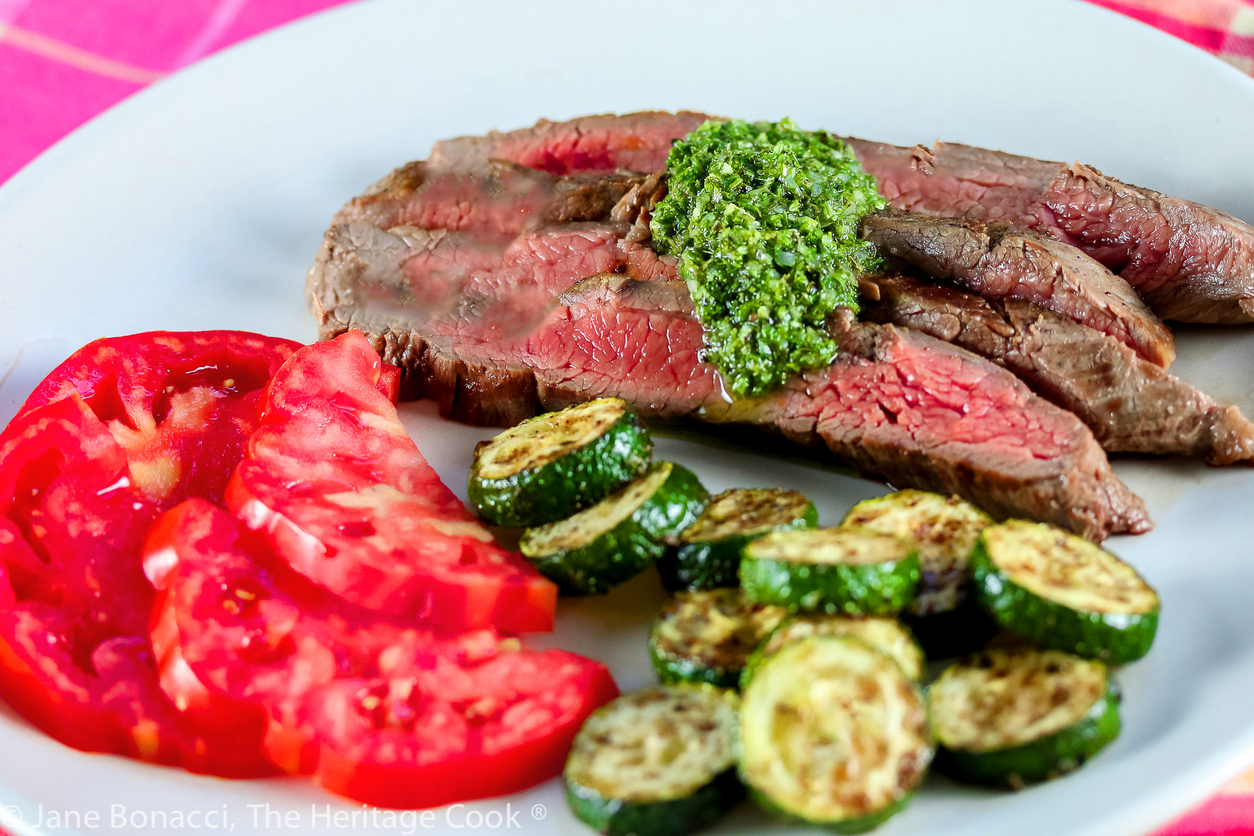 Slices of Flank Steak grilled and served with green herb Chimichurri sauce, sautéed zucchini, and sliced tomatoes © 2023 Jane Bonacci, The Heritage Cook. 