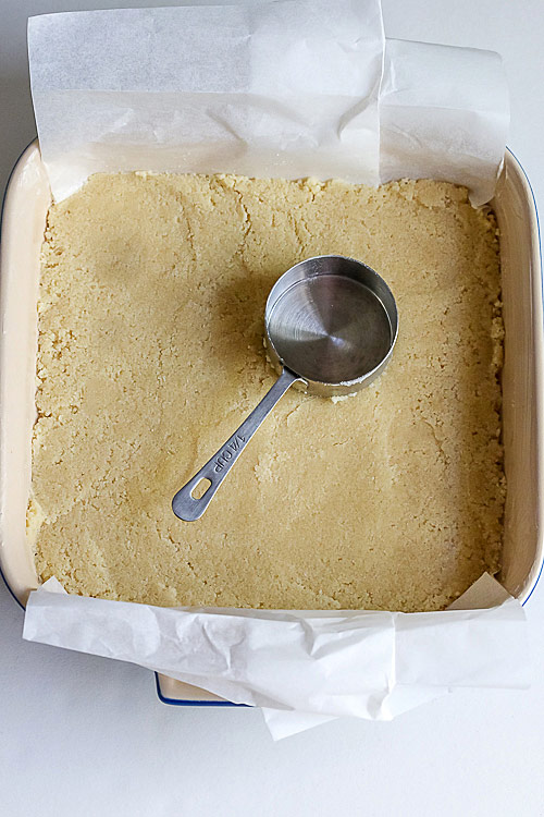 Using a measuring cup to press the crumb crust into the pan; The Most Refreshing Frozen Lemon Bars © 2017 Jane Bonacci, The Heritage Cook