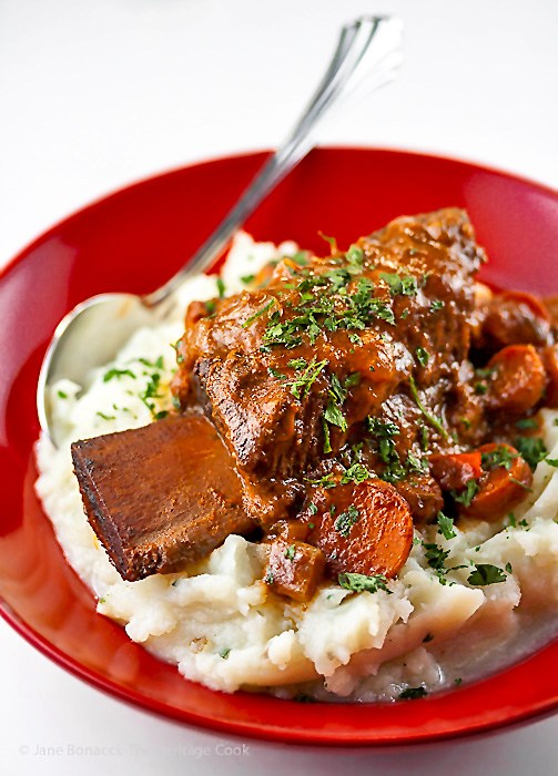 Red bowl filled with mashed potatoes and braised short ribs; 30 Warming Comfort Foods for Chilly Winter Days 2017 Jane Bonacci, The Heritage Cook