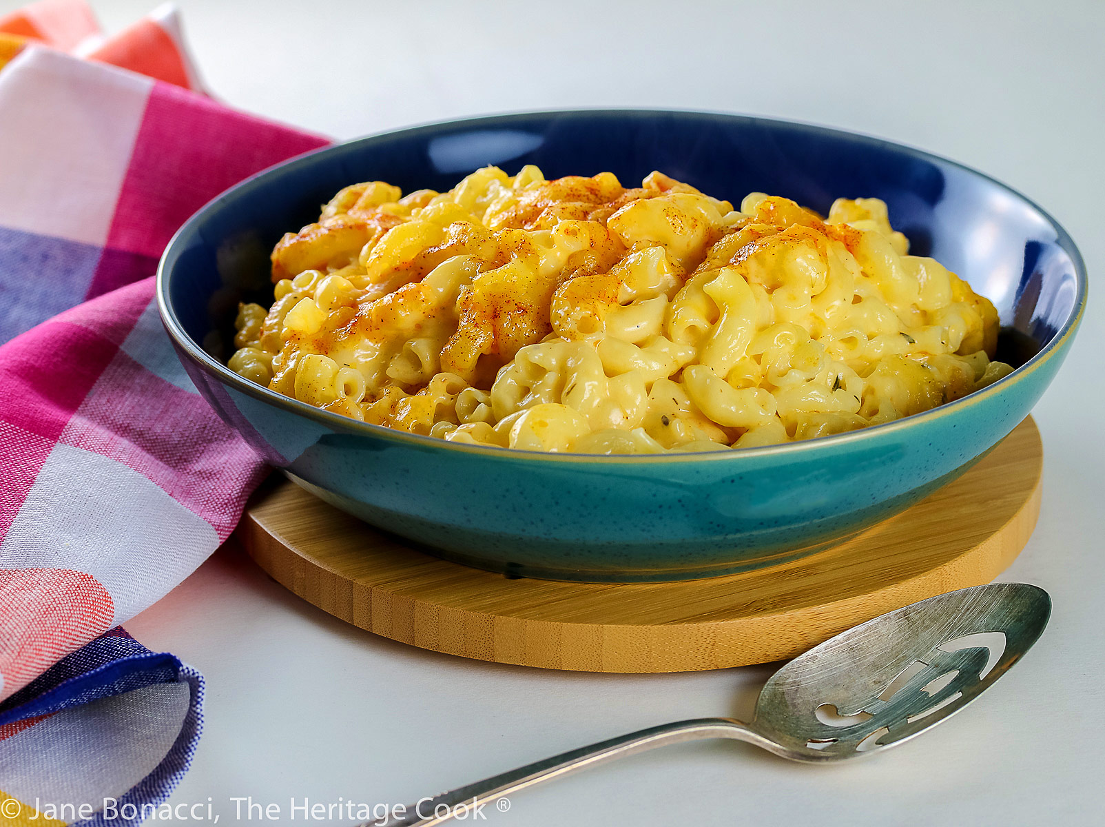 Blue and green bowl filled with creamy mac and cheese, sprinkled with paprika; Old Fashioned Creamy Mac and Cheese © 2023 Jane Bonacci, The Heritage Cook. 