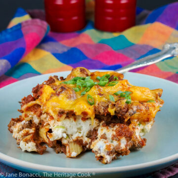 A large square piece of Mexican Sloppy Joe Lasagna Casserole on a pale blue plate topped with sliced green onions; a mash up of Mexican pasta and traditional lasagna for a delicious meal © 2023 Jane Bonacci, The Heritage Cook.
