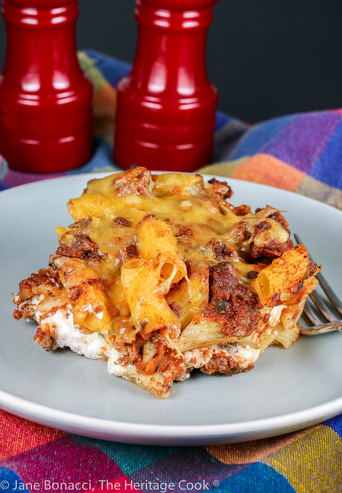 A large square piece of Mexican Sloppy Joe Lasagna Casserole on a pale blue plate topped with sliced green onions; a mash up of Mexican pasta and traditional lasagna for a delicious meal © 2023 Jane Bonacci, The Heritage Cook.