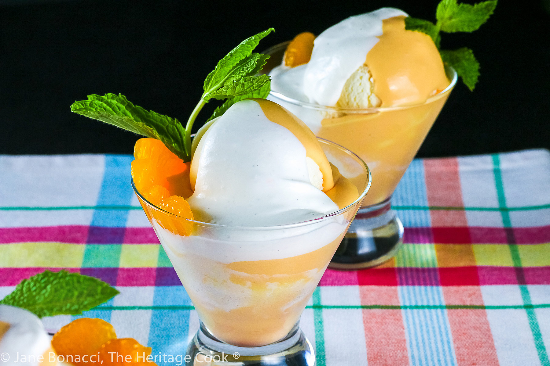 Vanilla ice cream with orange Creamsicle mousse in glass dish topped with whipped cream and a sprig of mint; on colorful cloth © 2023 Jane Bonacci, The Heritage Cook. 