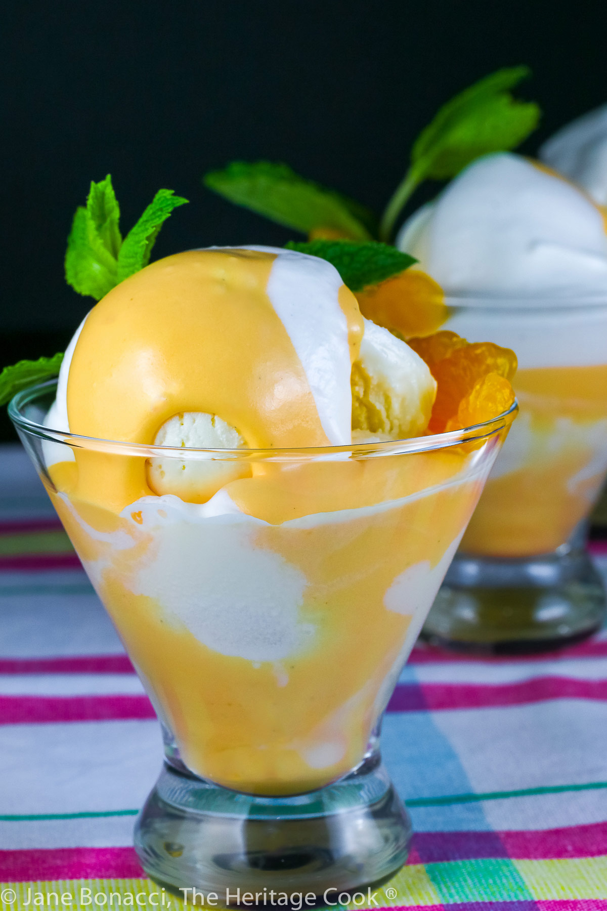 Vanilla ice cream with orange Creamsicle mousse in glass dish topped with whipped cream and a sprig of mint; on colorful cloth © 2023 Jane Bonacci, The Heritage Cook. 