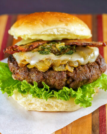 A grilled buffalo burger studded with chopped bacon fat and layered with lettuce, bacon, melted cheese, sauteed onions and Hatch green chiles; BBQ Green Chile Bacon Burgers © 2023 Jane Bonacci, The Heritage Cook.