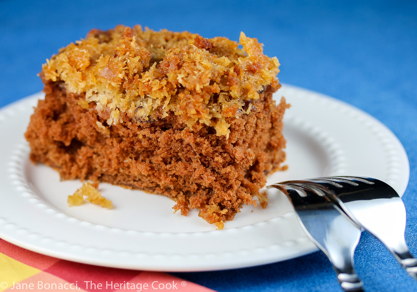 Square piece of cake with coconut/pecan frosting on a white plate; Cockeyed German Chocolate Cake © 2023 Jane Bonacci, The Heritage Cook.