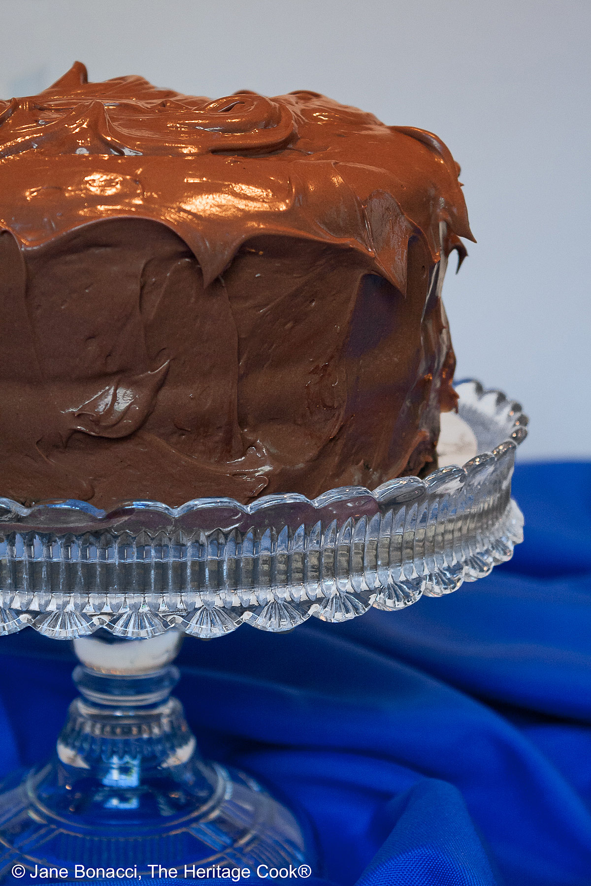 Whole Dark Chocolate Layer Cake with Chocolate Frosting on crystal cake stand with rich blue tablecloth; 2024 Jane Bonacci, The Heritage Cook.
