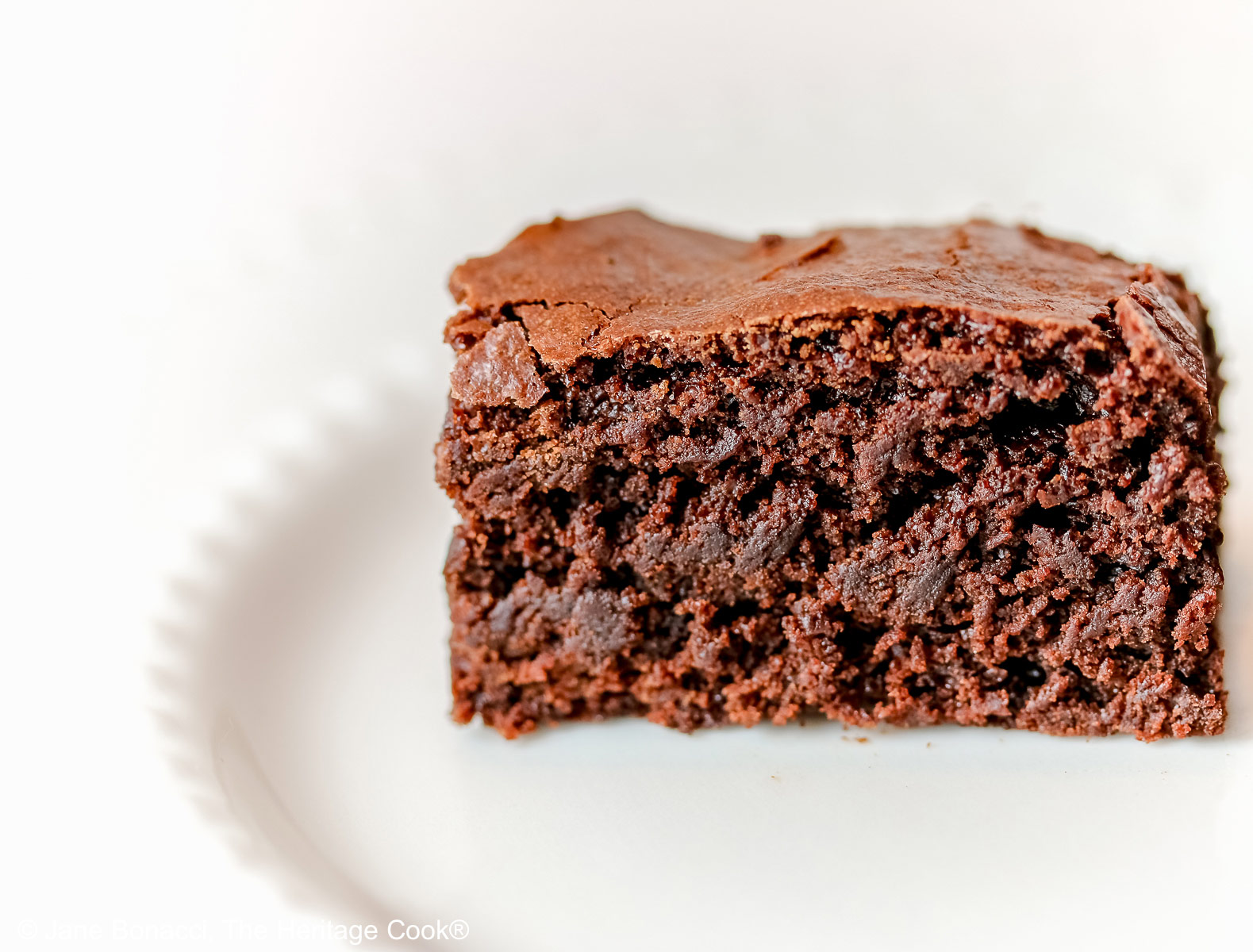 Close up of the side view of a single brownie on a white plate. 