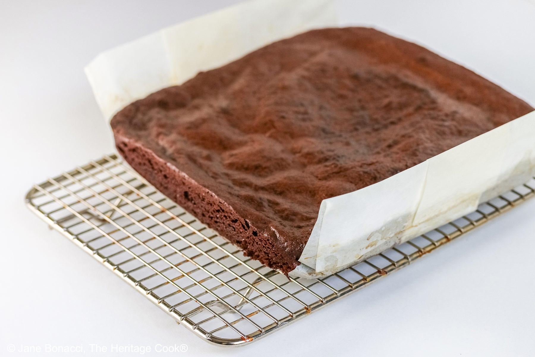 Whole block of brownies with a parchment sling, sitting on a wire cooling rack. 