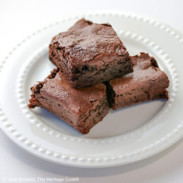 The Best Chewy Brownies, rich and so chocolatey, stacked on a white plate with two rows of white pearls, sitting on a white background; some shots of the cookbook, “Bittersweet” by Alice Medrich; © 2025 Jane Bonacci, The Heritage Cook.
